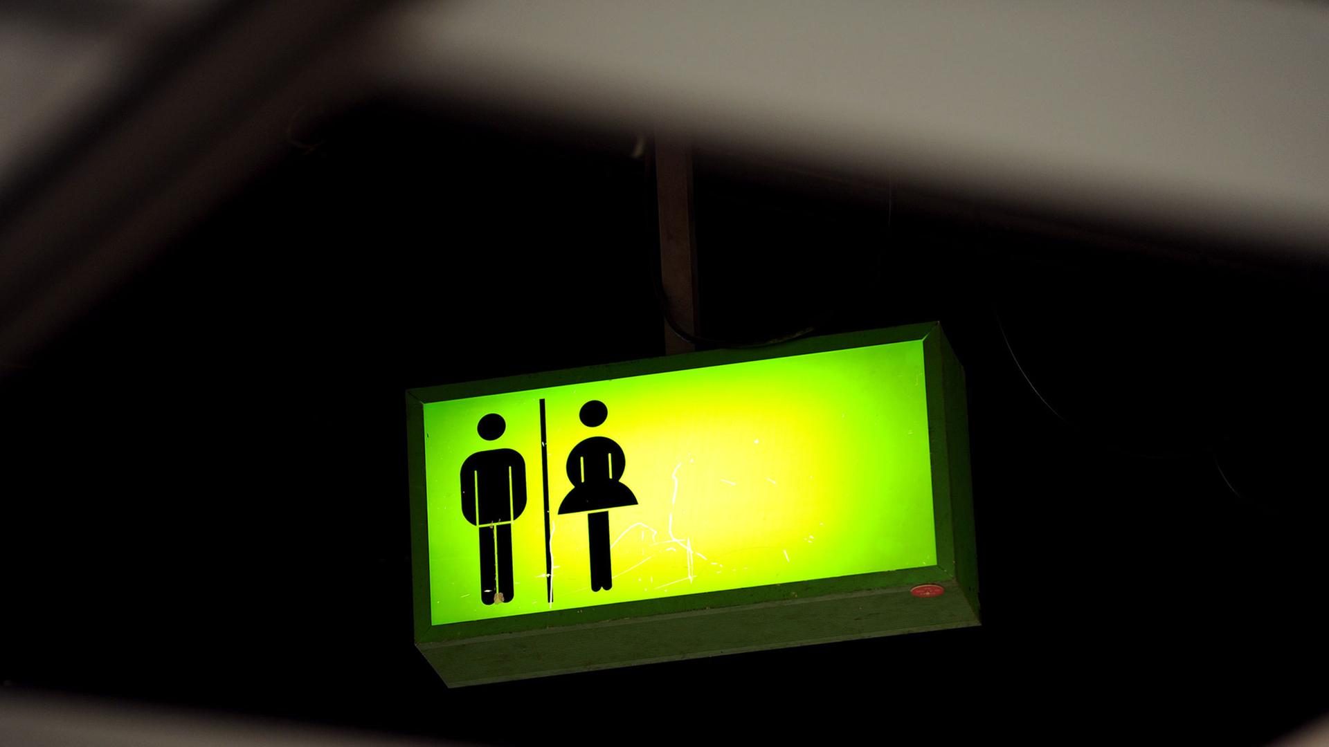 Ein grün leuchtendes Toiletten-Hinweisschild hängt auf dem Messegelände in Frankfurt am Main unter der Decke Ein grün leuchtendes Toiletten-Hinweisschild hängt auf dem Messegelände in Frankfurt am Main unter der Decke