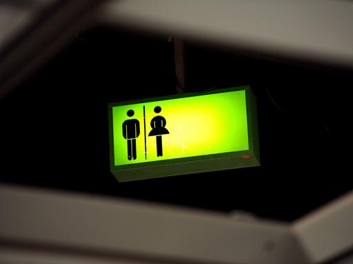 Ein grün leuchtendes Toiletten-Hinweisschild mit einem weiblichen und einem männlichen Piktogramm