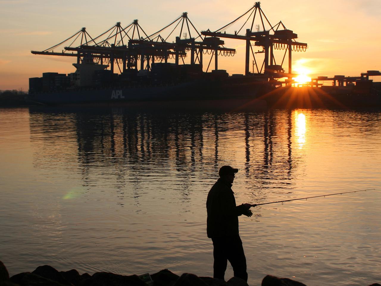 Ein Mann angelt am während des Sonnenuntergangs vor dem Container-Terminal Altenwerder (CTA) im Hamburger Hafen. Ein Mann angelt am während des Sonnenuntergangs vor dem Container-Terminal Altenwerder (CTA) im Hamburger Hafen.