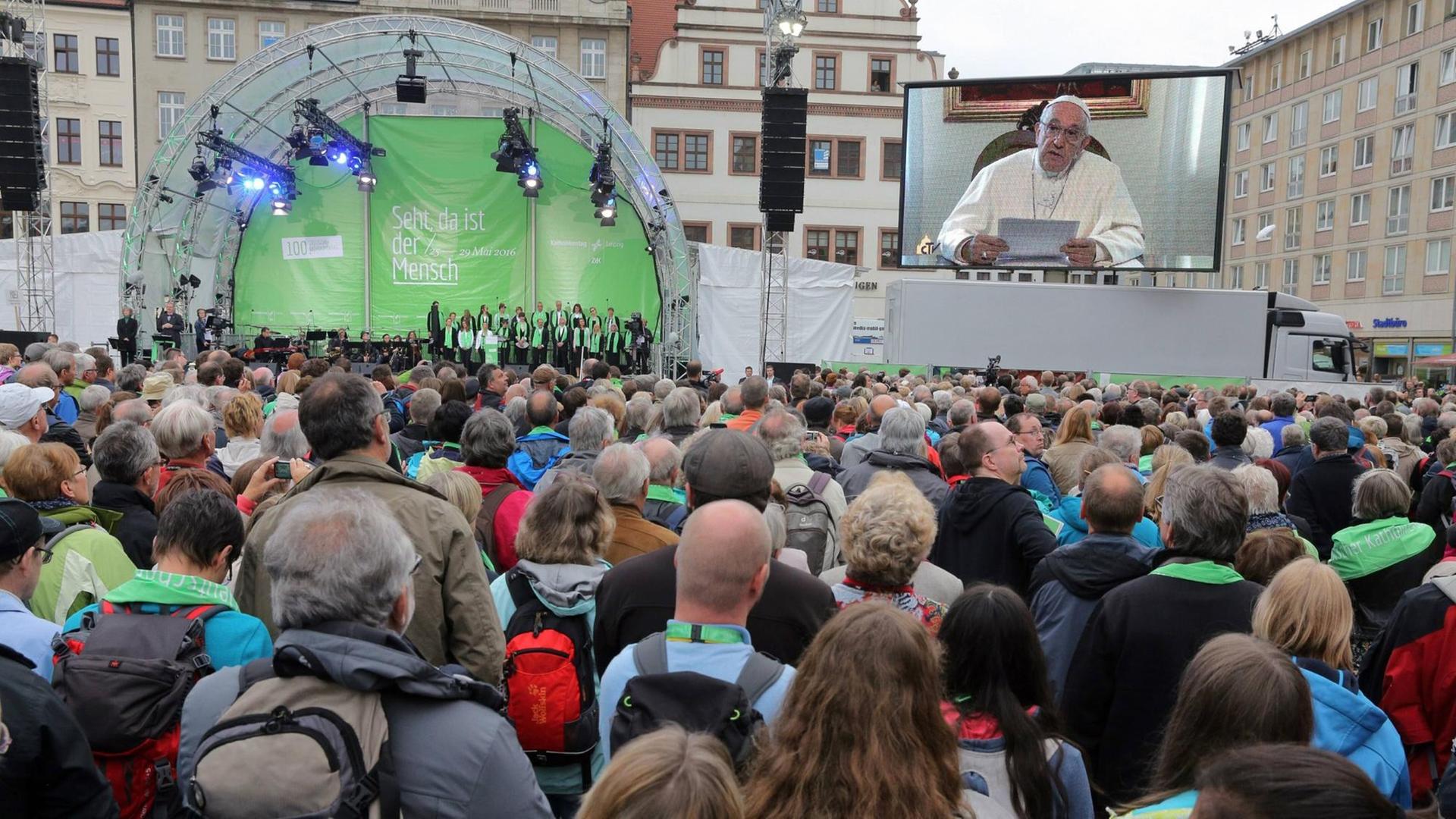 Papst Franziskus wendet sich mit einer Videobotschaft an die Teilnehmer des Katholikentags in Leipzig, die vor einer Bühne stehen.