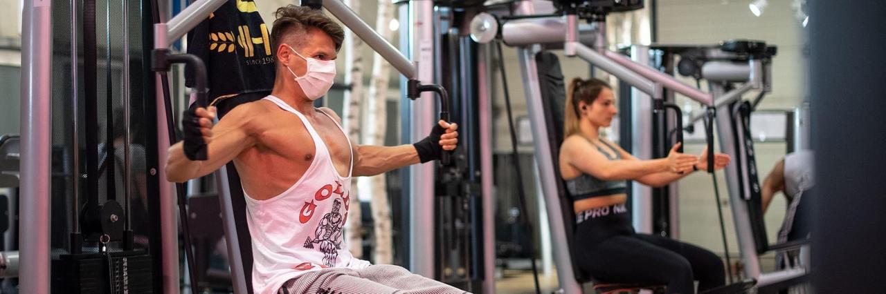 Ein Mann mit Mundschutz trainiert in einem Fitnessstudio an einer Brustpresse. Ein Mann mit Mundschutz trainiert in einem Fitnessstudio an einer Brustpresse.