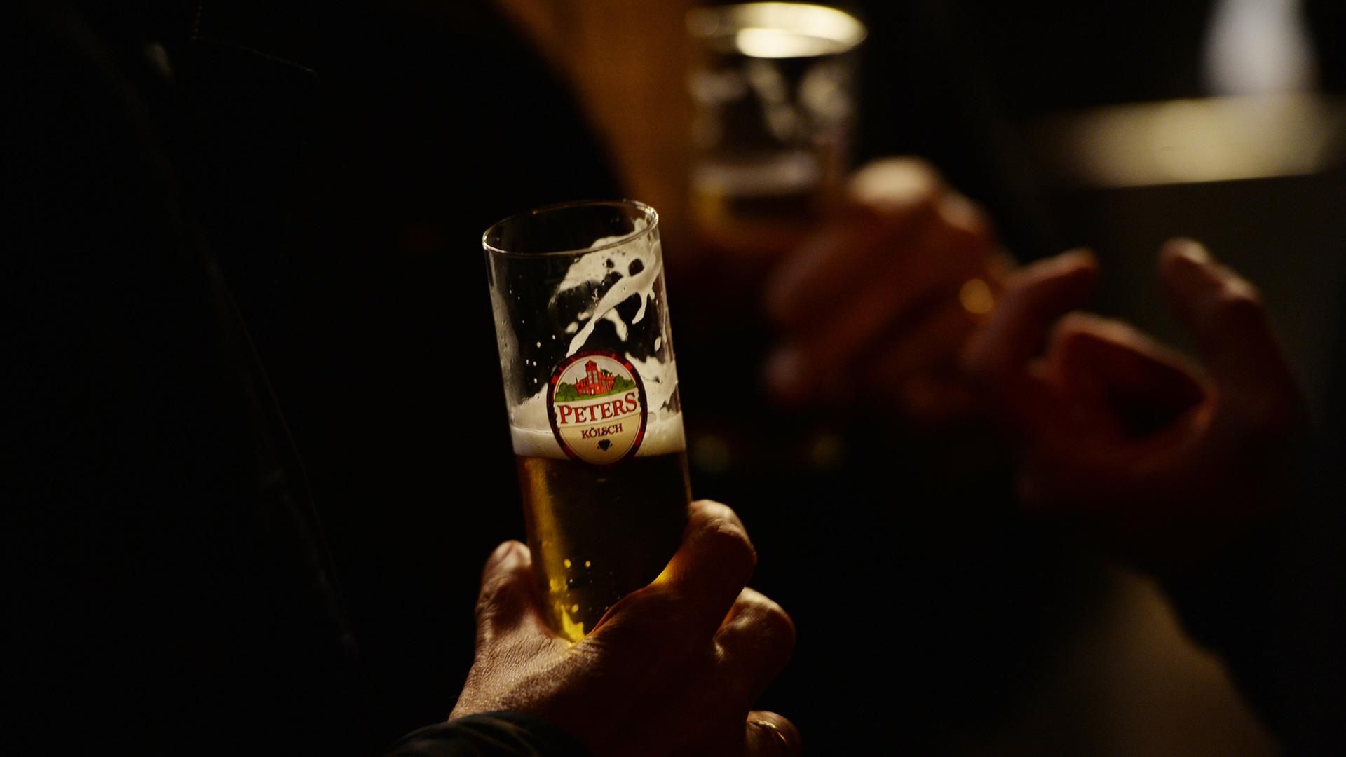 Ein Mann hält ein Kölsch-Glas in der Hand. Ein Mann hält ein Kölsch-Glas in der Hand.