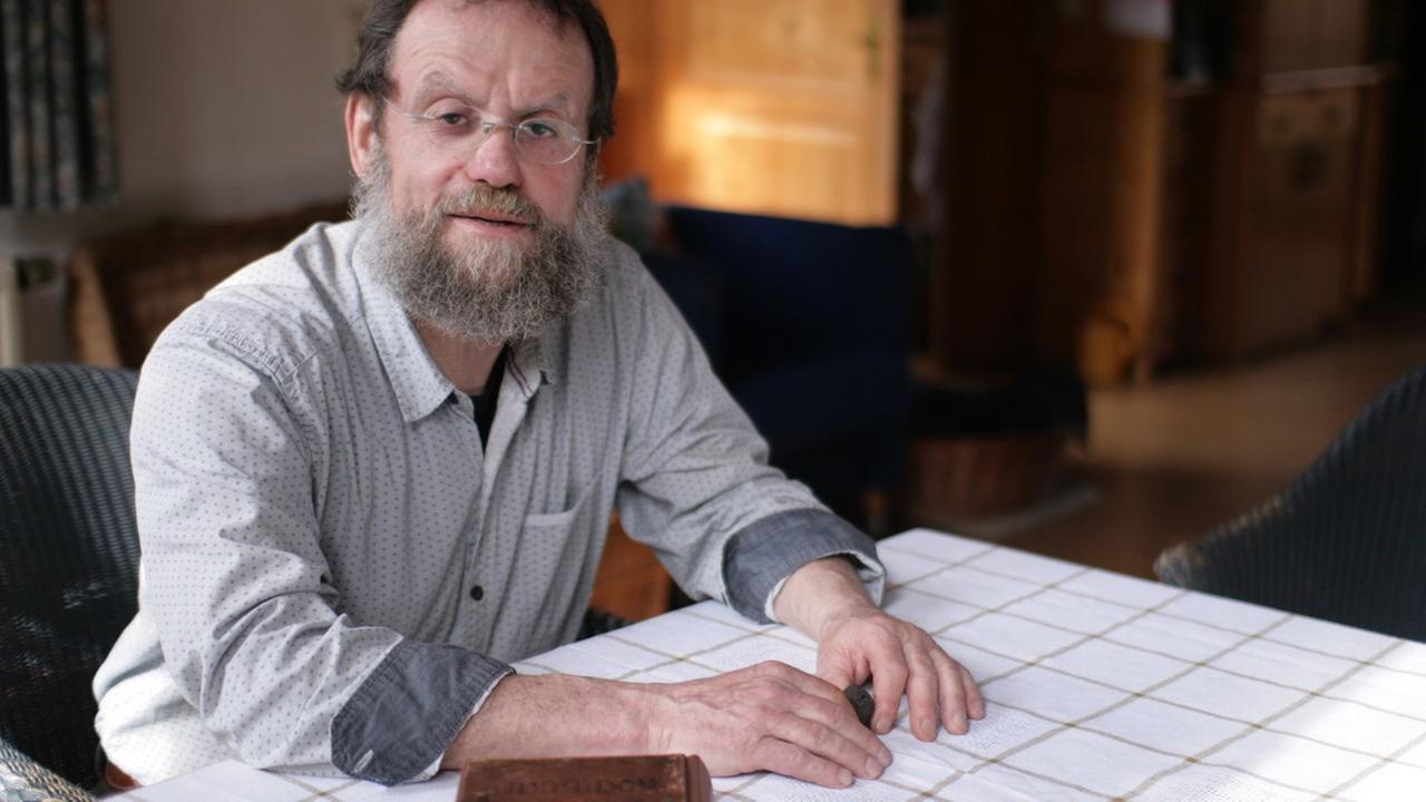 Josef Valentin Herrmann sitzt an einem Tisch auf dem ein historisches Kochbuch liegt, in der Hand ein Trüffel Josef Valentin Herrmann sitzt an einem Tisch auf dem ein historisches Kochbuch liegt, in der Hand ein Trüffel