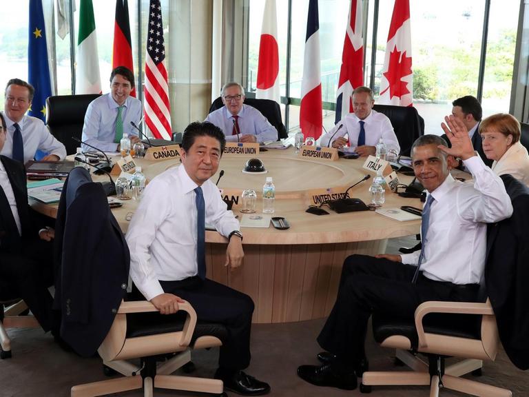 Die Staats- und Regierungschef der G7-Staaten sitzen gemeinsam an einem runden Tisch, Obama winkt in die Kamera.