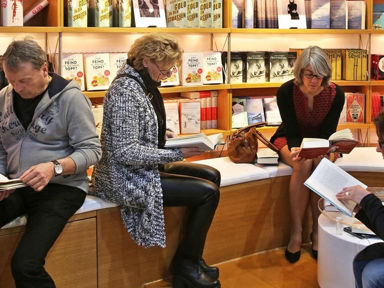 Vier Frauen und ein Mann sitzen vor einer Bücherwand und lesen.