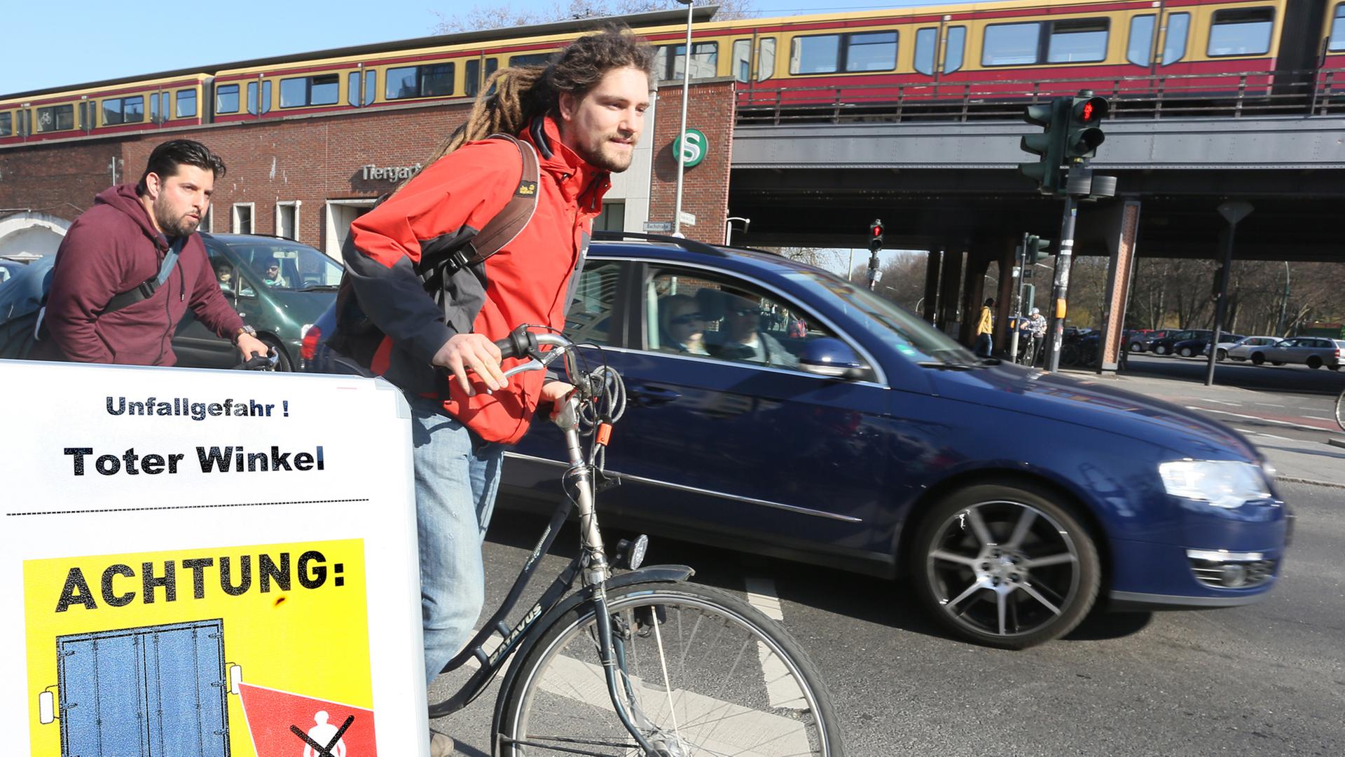 Fahrradfahrer fahren auf einem Fahrradweg an einer Kreuzung in Berlin geradeaus, während ein Auto rechts abbiegen will, davor weist ein Schild über den Toten Winkel als Unfallgefahr hin. Fahrradfahrer fahren auf einem Fahrradweg an einer Kreuzung in Berlin geradeaus, während ein Auto rechts abbiegen will, davor weist ein Schild über den Toten Winkel als Unfallgefahr hin.