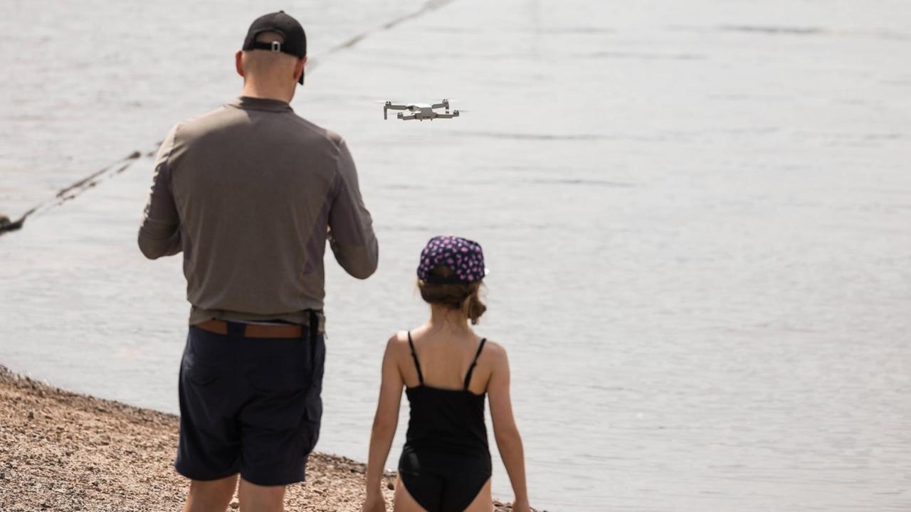 Rückansicht von Vater und Tochter mit fliegender Drohne am Schluchsee Rückansicht von Vater und Tochter mit fliegender Drohne am Schluchsee