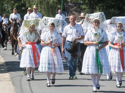 Junge Frauen und Männer in sorbischer Tracht nehmen im Spreewald am traditionellen Hahnrupfen teil.
