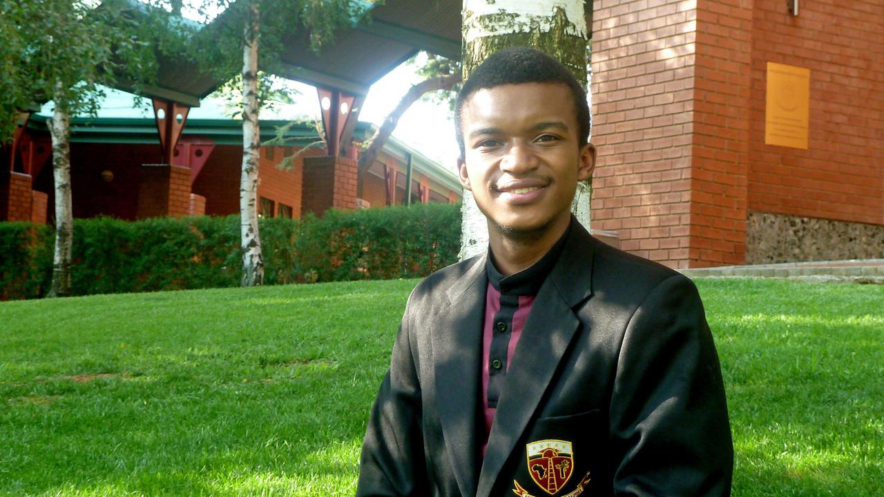 Ein junger Afrikaner steht in Schuluniform mit Jackett und Schulabzeichen auf dem Campusrasen. Ein junger Afrikaner steht in Schuluniform mit Jackett und Schulabzeichen auf dem Campusrasen.