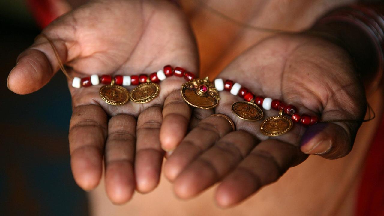 Frauenhände die einer rotweiße Perlenkette halten.