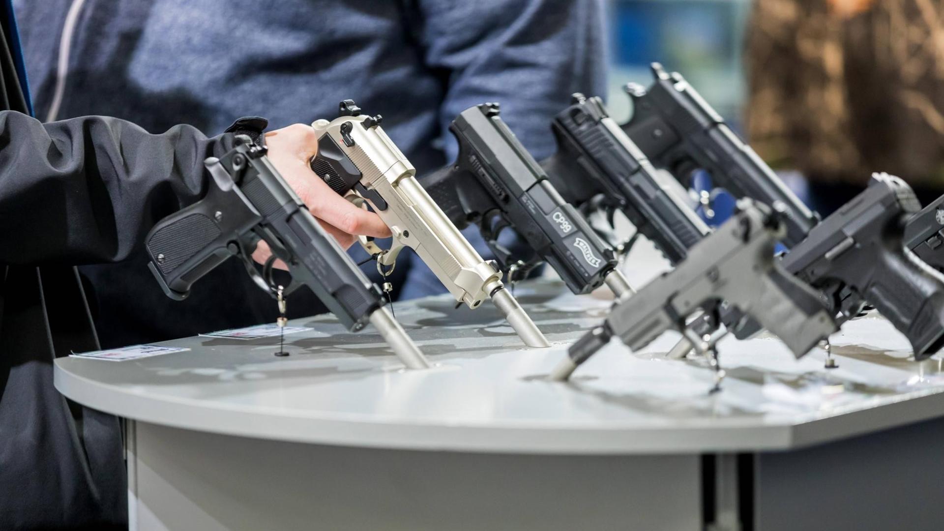 Februar 2018: Auf der Messe "Jagd & Hund" in den Dortmunder Westfalenhallen sind auf einem Tisch mehrere Pistolen ausgestellt. Jemand umschließt eine davon mit der Hand. Februar 2018: Auf der Messe "Jagd & Hund" in den Dortmunder Westfalenhallen sind auf einem Tisch mehrere Pistolen ausgestellt. Jemand umschließt eine davon mit der Hand.