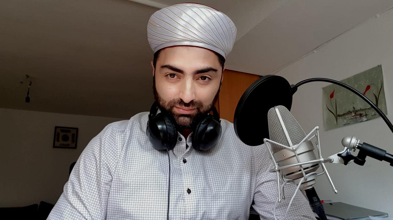 Porträt von Ömer Aslan, Dozent für die Kunst der Koranrezitation an der Goethe Universität Frankfurt, im weißen Hemd und mit weißem Turban vor einem Mikrofon sitzend