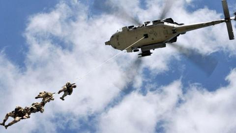 Spezialkräfte der Navy Seals im Einsatz. Ein Hubschrauber in der Luft . Drei Soldaten hängen an einem Seil während des Fluges unterhalb des Hubschraubers