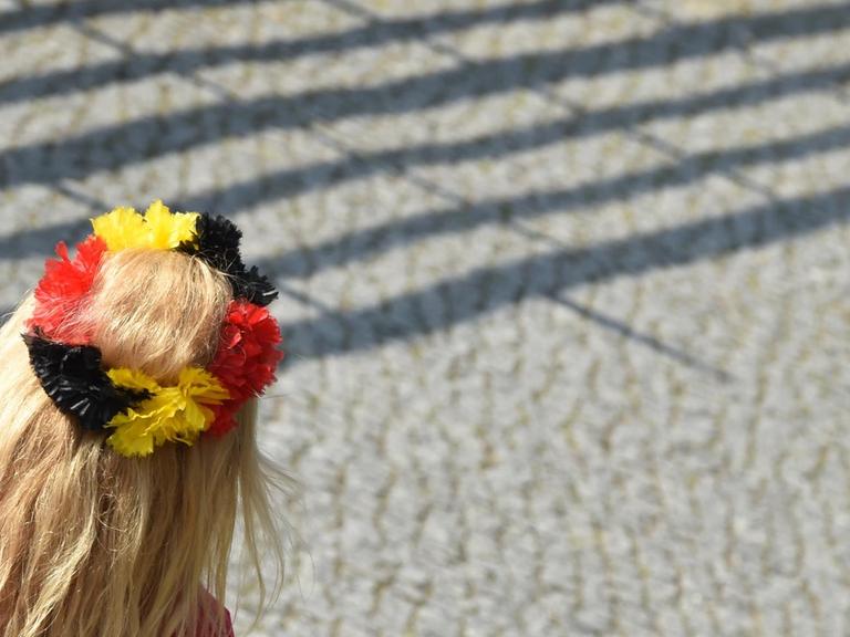 Eine junge Frau kommt mit einem Haarkranz mit schwarz-rot-goldenen Blüten am 15.07.2014 in Berlin zum Empfang der Fußball-Nationalmannschaft.