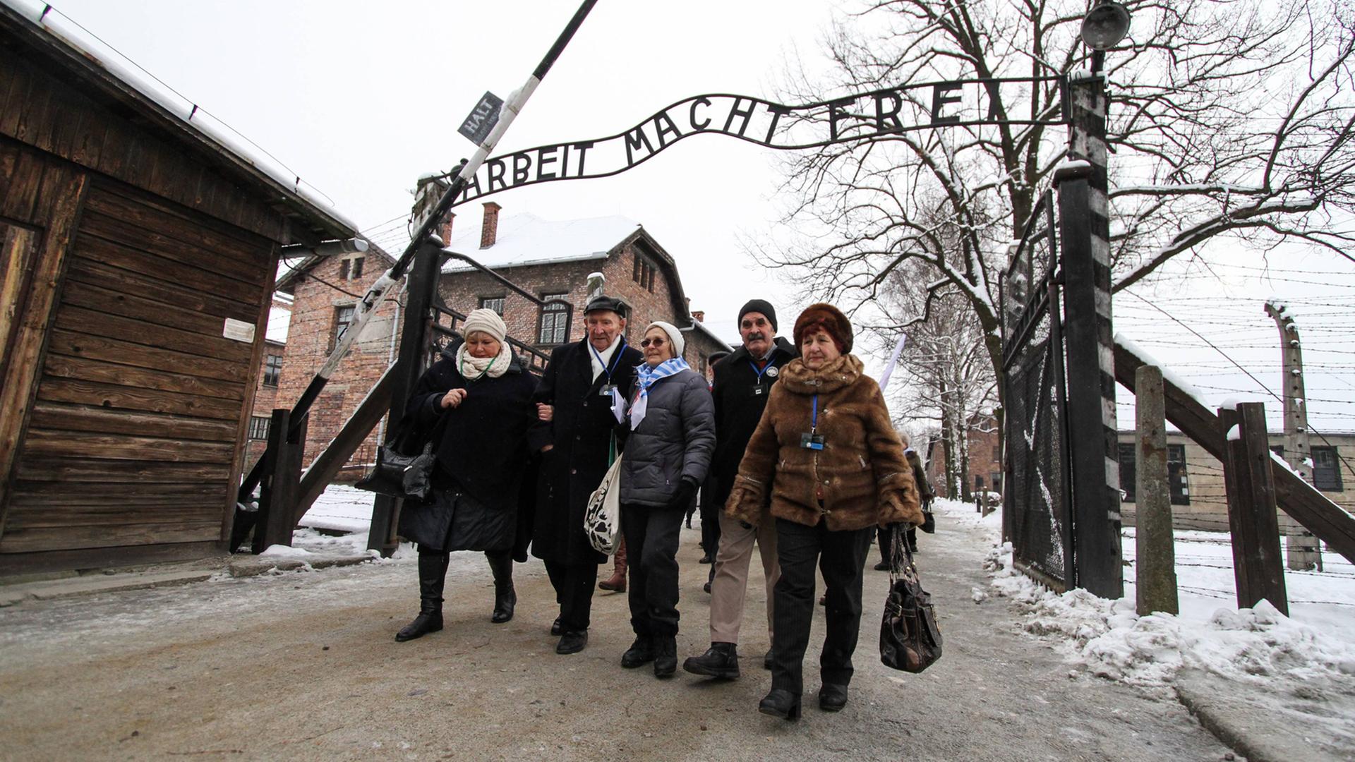 Überlebende des Konzentrationslagers Auschwitz vor dem Eingang mit dem Schriftzug "Arbeit macht frei". Überlebende des Konzentrationslagers Auschwitz vor dem Eingang mit dem Schriftzug "Arbeit macht frei".