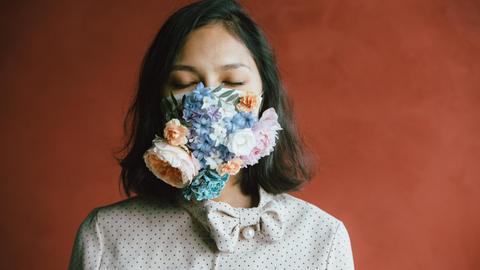 Eine Frau trägt eine Atemschutzmaske, die über und über mit Blüten bedeckt ist.