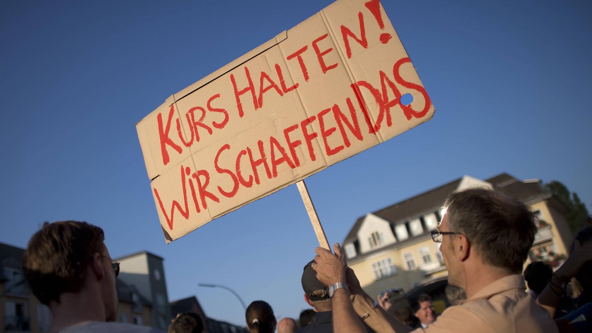 Ein Mann hält ein Schild hoch mit der Aufschrift "Wir schaffen das". Ein Mann hält ein Schild hoch mit der Aufschrift "Wir schaffen das".