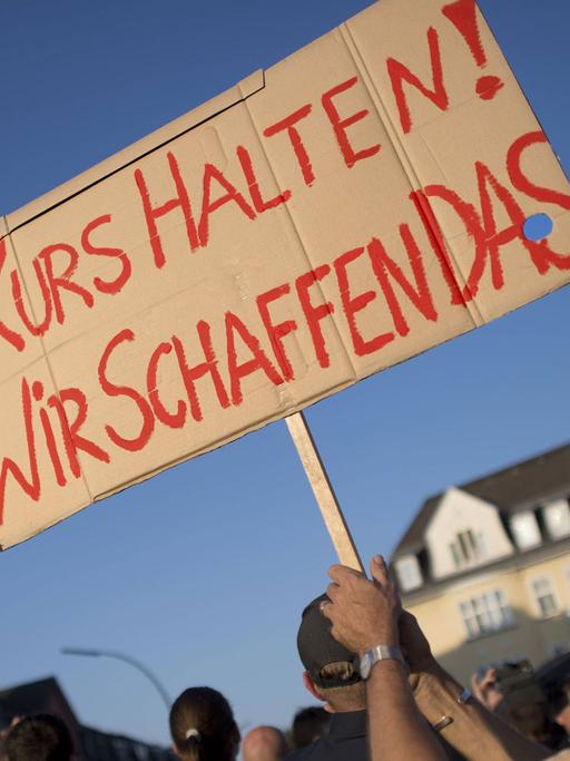 Ein Mann hält ein Schild hoch mit der Aufschrift "Wir schaffen das".