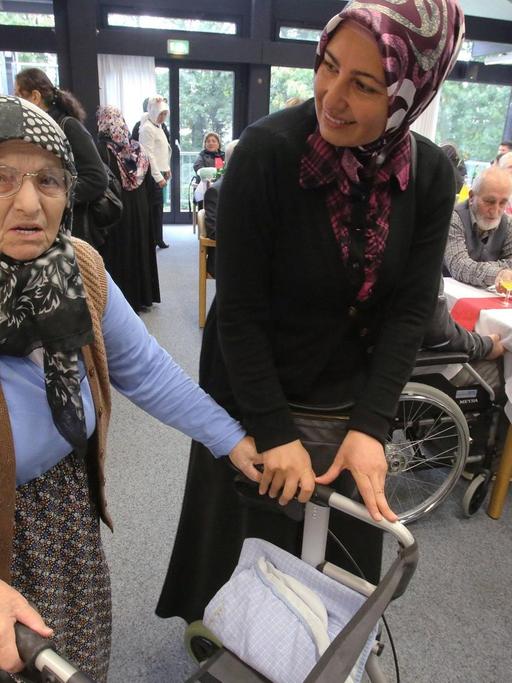 Muslimische Pflegerin hilft einer Seniorin mit Rollator im multikulturellen Seniorenzentrum des deutschen Roten Kreuzes (DRK), Haus am Sandberg in Duisburg.