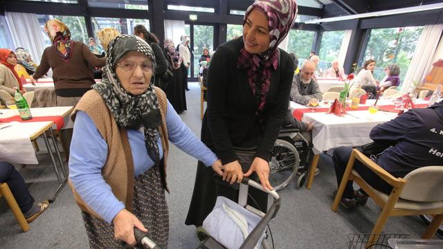 Muslimische Pflegerin hilft einer Seniorin mit Rollator im multikulturellen Seniorenzentrum des deutschen Roten Kreuzes (DRK), Haus am Sandberg in Duisburg.