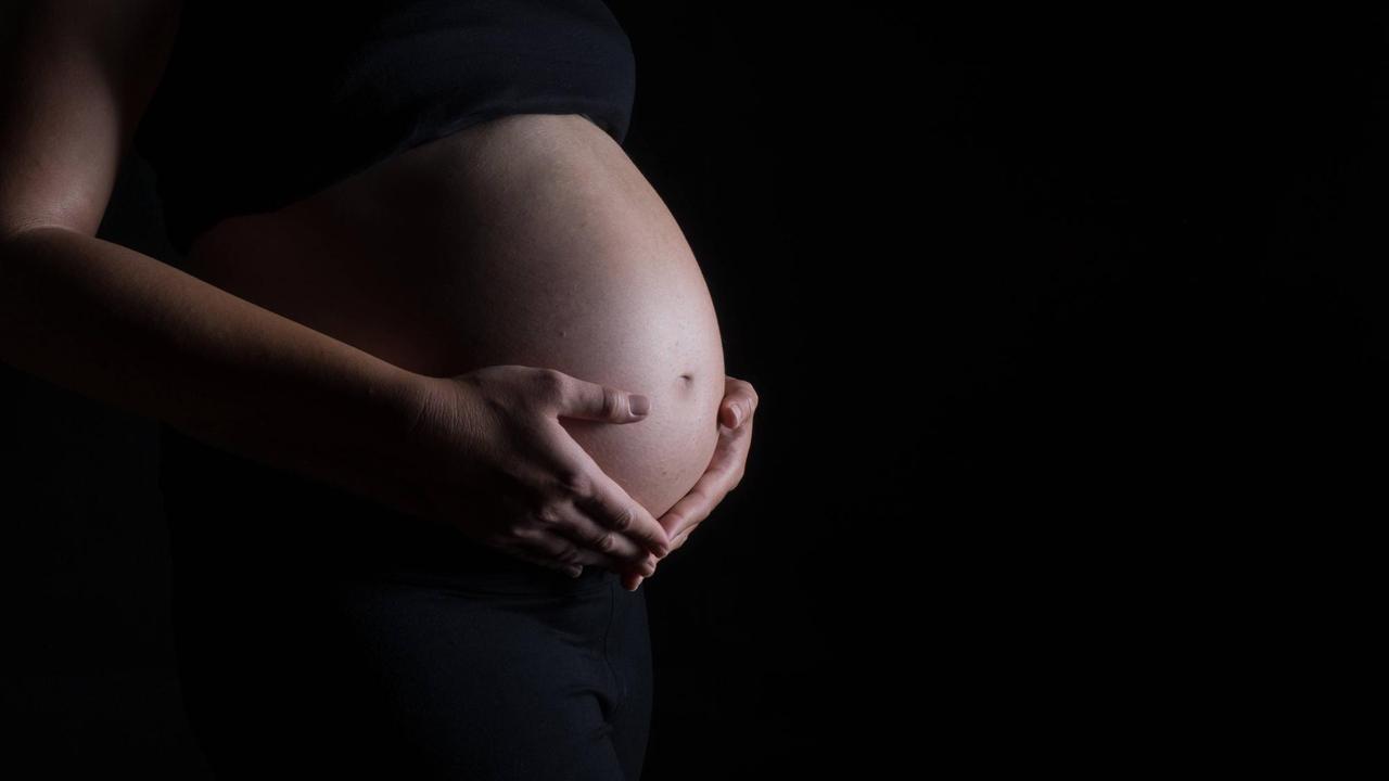 Eine schwangere Frau hält ihren Bauch. 