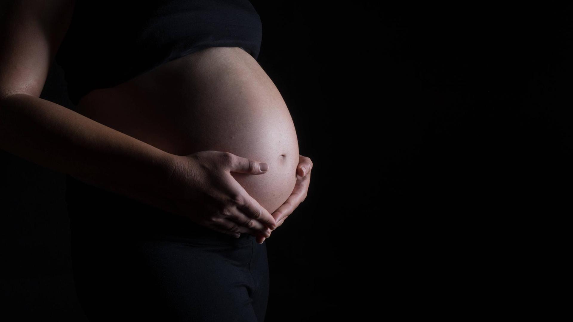 Eine schwangere Frau hält ihren Bauch. Eine schwangere Frau hält ihren Bauch.