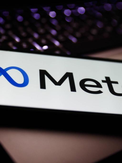 Das neue Logo von Meta (ehemals Facebook) auf einem Smartphone, das auf einem Laptop liegt.