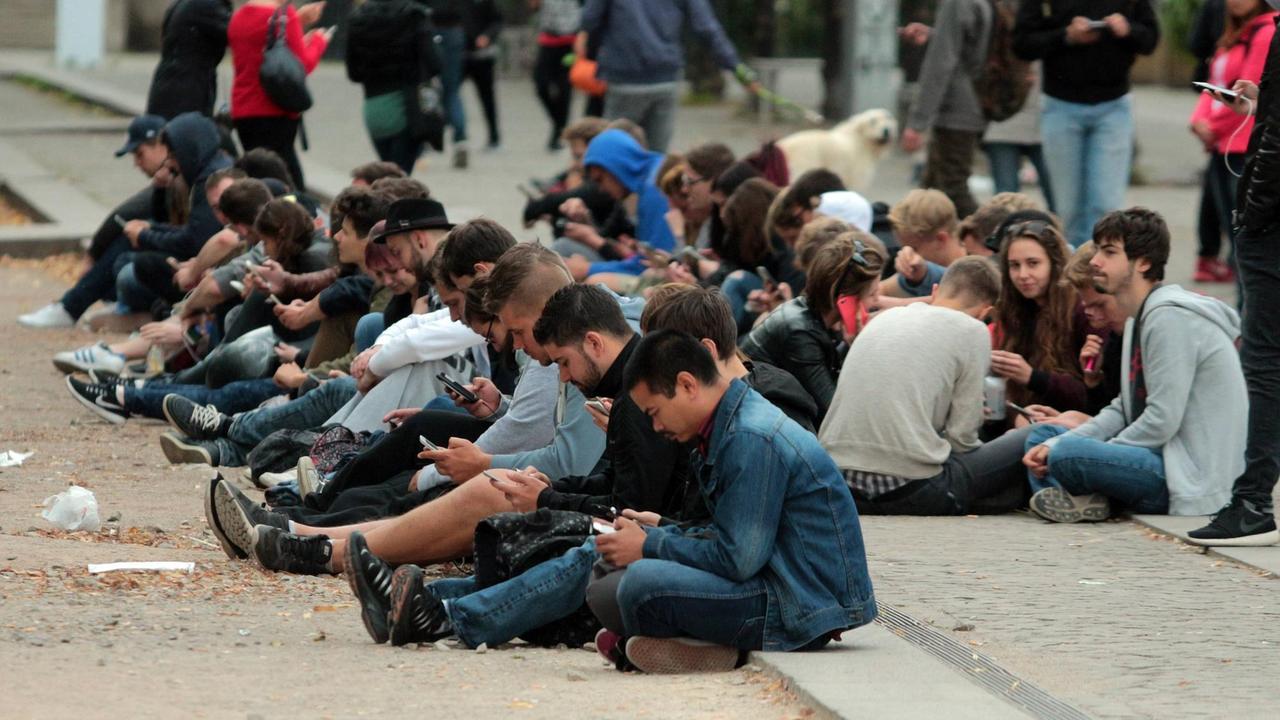 Im Berliner Lustgarten sitzen junge Menschen auf dem Boden und starren auf die Displays ihrer Smartphones. Im Berliner Lustgarten sitzen junge Menschen auf dem Boden und starren auf die Displays ihrer Smartphones.