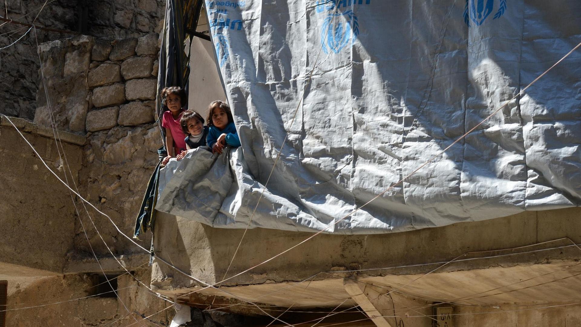 Kinder in der vom Krieg zerstörten Stadt Aleppo schauen hinter der Plane eines zerstörten Hauses hervor. Kinder in der vom Krieg zerstörten Stadt Aleppo schauen hinter der Plane eines zerstörten Hauses hervor.