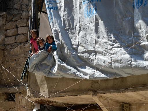 Kinder in der vom Krieg zerstörten Stadt Aleppo schauen hinter der Plane eines zerstörten Hauses hervor.