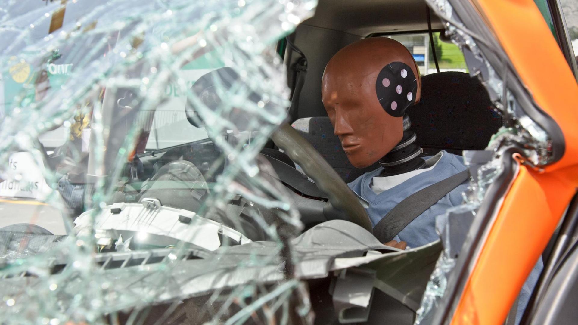 Eine Crashtestpuppe sitzt nach einer Frontalkollision mit einem anderen PKW hinter zerborstetem Glas und Metall in einem Versuchsfahrzeug. Eine Crashtestpuppe sitzt nach einer Frontalkollision mit einem anderen PKW hinter zerborstetem Glas und Metall in einem Versuchsfahrzeug.