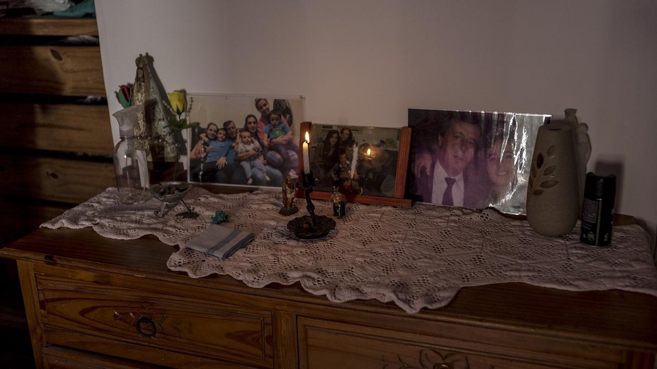 Auf einer Kommode stehen auf einem weißen Deckchen vor einer brennenden Kerze mehrere gerahmte Fotos, die u.a. den Vater mit der Tochter zeigen. Auf einer Kommode stehen auf einem weißen Deckchen vor einer brennenden Kerze mehrere gerahmte Fotos, die u.a. den Vater mit der Tochter zeigen.