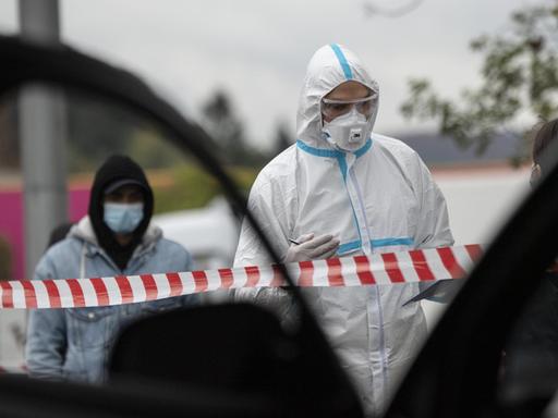 In einen Ganzkörper-Schutzanzug gekleidet ist ein Mitarbeiter eines Corona-Testzentrums auf dem Messegelände in Marburg.