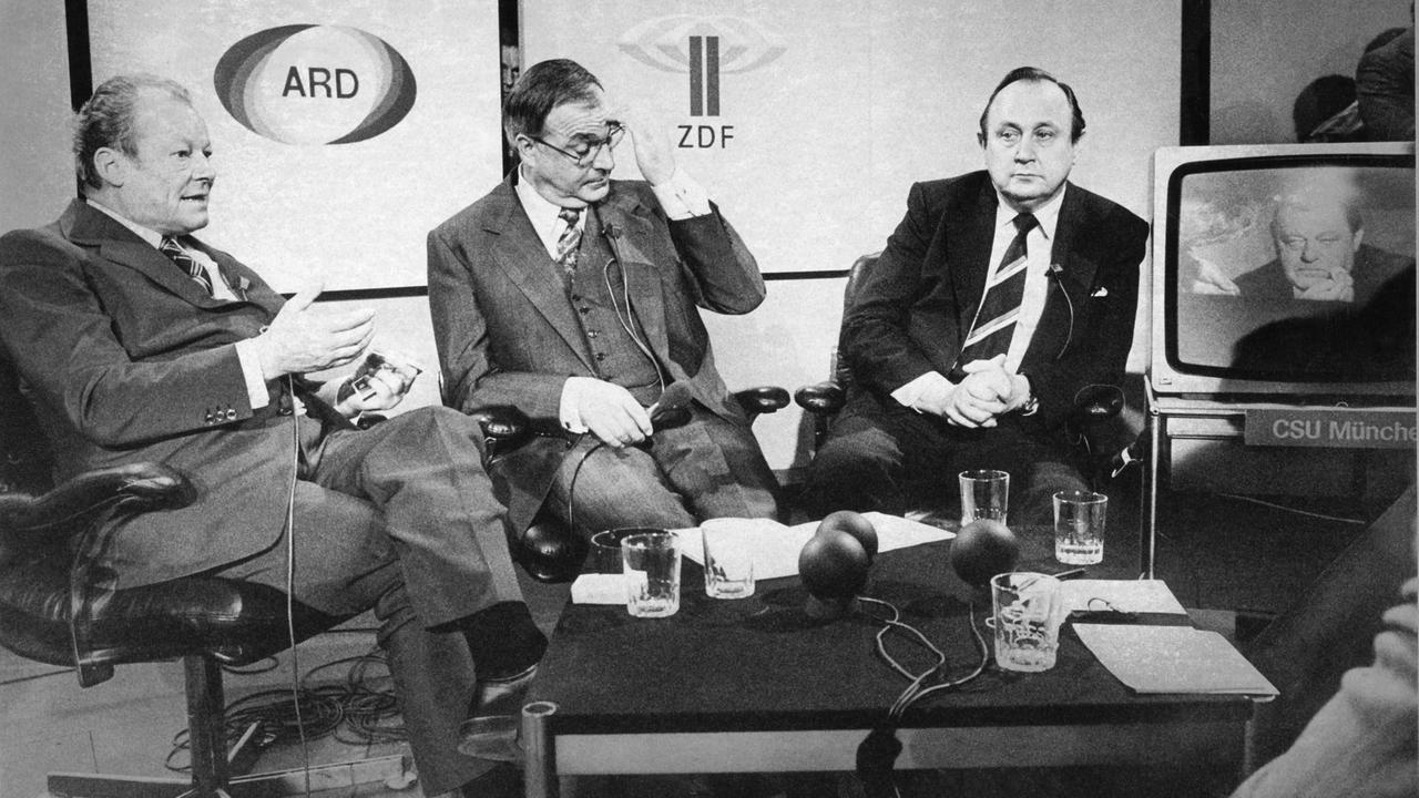 (l-r): Die Parteivorsitzenden Willy Brandt (SPD), Helmut Kohl (CDU), Hans-Dietrich Genscher (FDP) und per Zuschaltung auf dem Bildschirm Franz Josef Strauß (CSU) diskutieren am 3. Oktober 1976 in Bonn die Wahl.