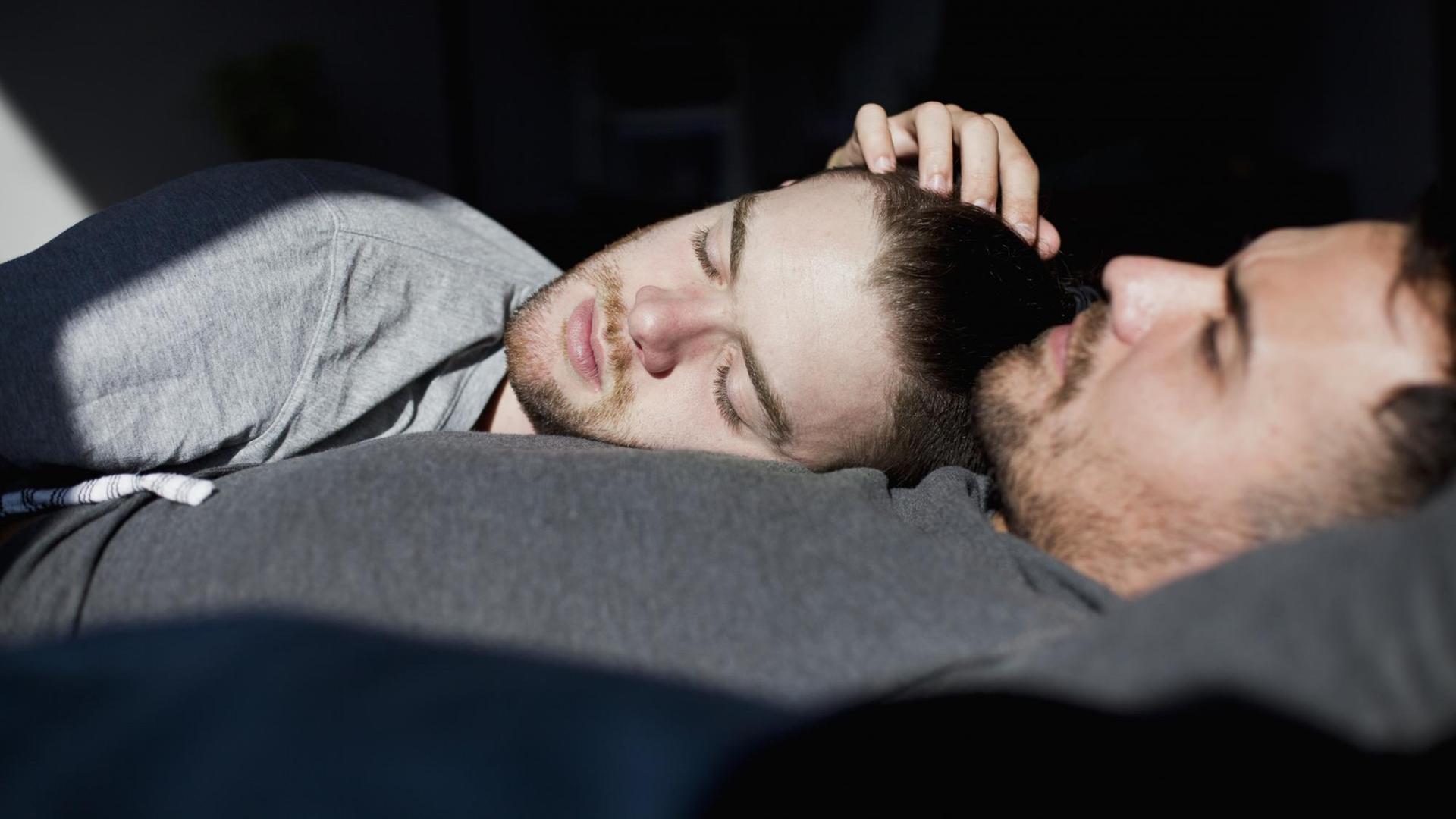 Ein schwules Paar liegt mit geschlossenen Augen im Bett und die Sonne scheint ihnen ins Gesicht. Ein schwules Paar liegt mit geschlossenen Augen im Bett und die Sonne scheint ihnen ins Gesicht.