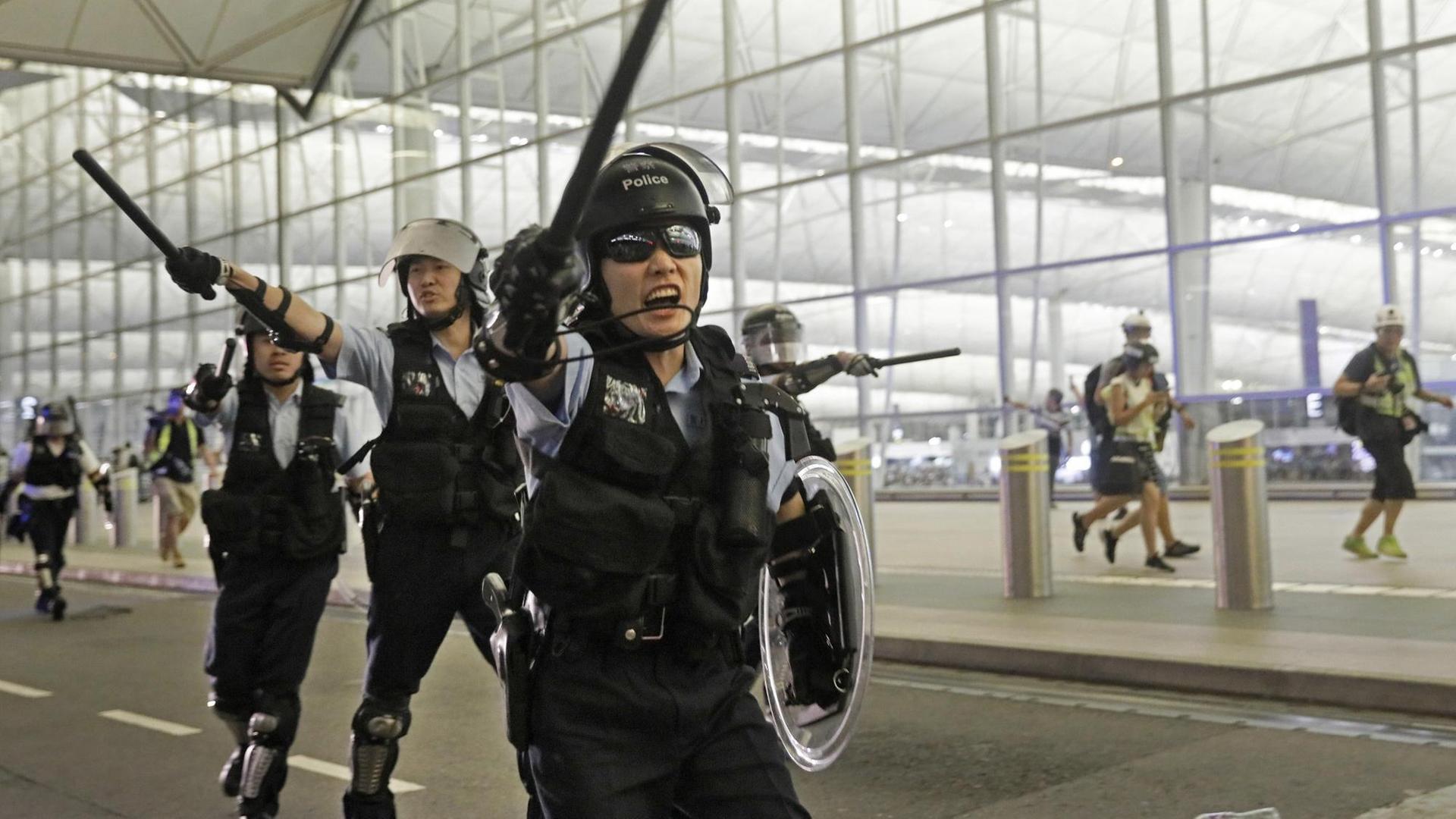 Polizisten mit Schlagstöcken schreien Demonstranten im Hongkonger Flughafen an.