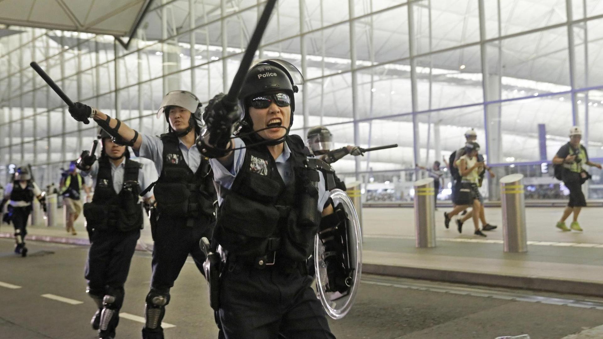 Polizisten mit Schlagstöcken schreien Demonstranten im Hongkonger Flughafen an. Polizisten mit Schlagstöcken schreien Demonstranten im Hongkonger Flughafen an.