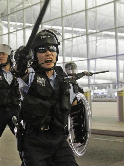Polizisten mit Schlagstöcken schreien Demonstranten im Hongkonger Flughafen an.