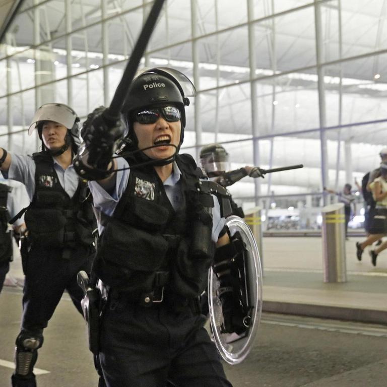 Polizisten mit Schlagstöcken schreien Demonstranten im Hongkonger Flughafen an. 