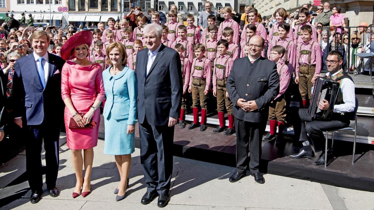 Horst Seehofer steht neben Königin Maxima und Willem-Alexander, hinter ihnen der Tölzer Knabenchor auf einer Bühne in rot-weiß karierten Hemden und Lederhosen. Horst Seehofer steht neben Königin Maxima und Willem-Alexander, hinter ihnen der Tölzer Knabenchor auf einer Bühne in rot-weiß karierten Hemden und Lederhosen.
