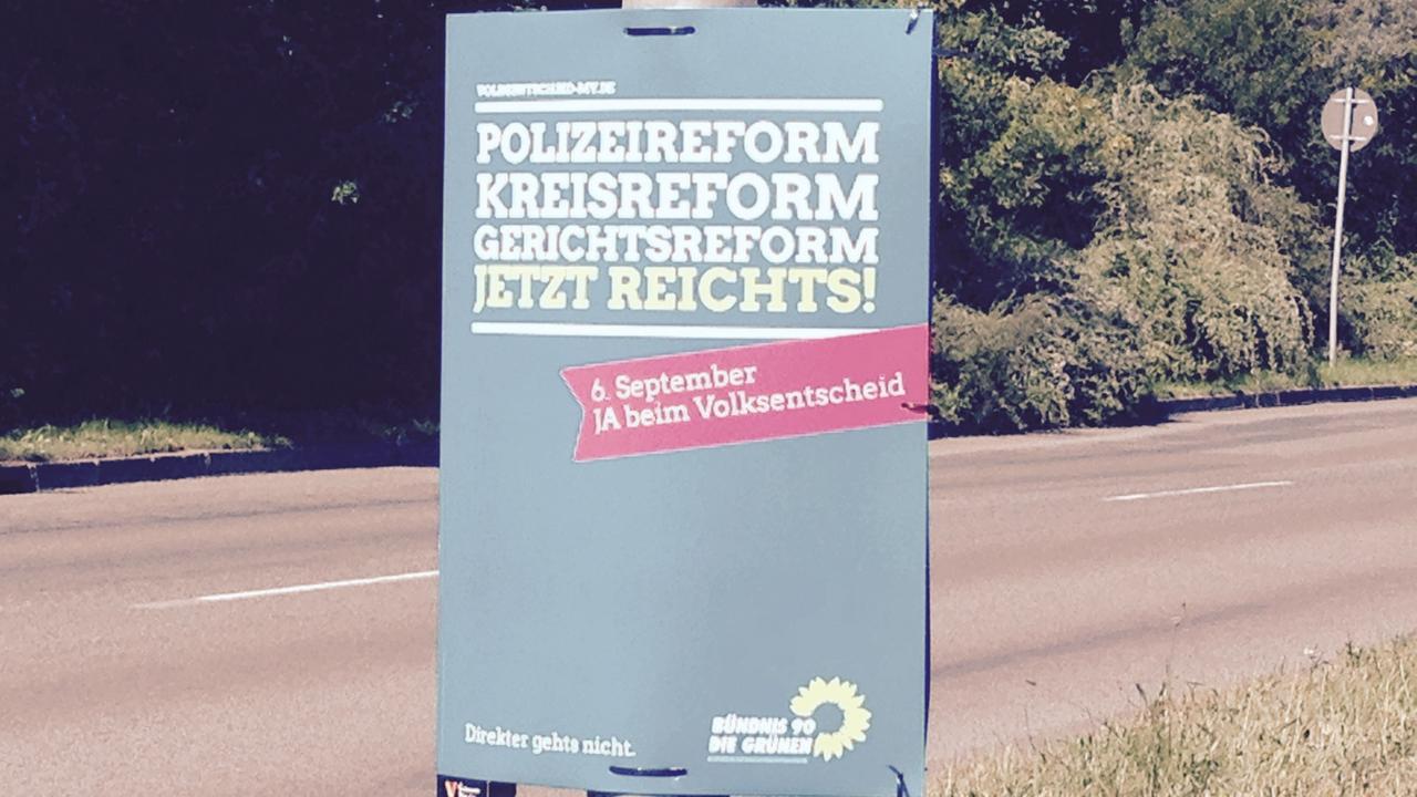Plakat der Grünen an einem Laternenpfahl am Straßenrand mit der Aufschrift: Polizeireform, Kreisreform, Gerichtsreform - jetzt reicht's! 6. September - Ja beim Volksentscheid.