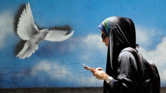 Straßenszene in Teheran: Eine Frau läuft vor einer Wand entlang, auf der eine Taube aufgemalt ist
