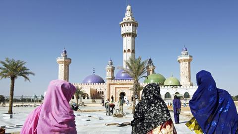 Vor der Großen Moschee in der Stadt Touba sind drei Frauen zu sehen, die auf das Gebäude zugehen.