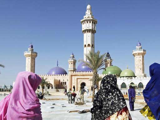 Vor der Großen Moschee in der Stadt Touba sind drei Frauen zu sehen, die auf das Gebäude zugehen.