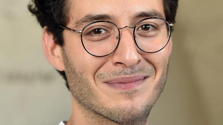 Schauspieler Mehmet Ateşçi. Ein junger Mann mit kurzen dunklen Haare und Brille lächelt in die Kamera.