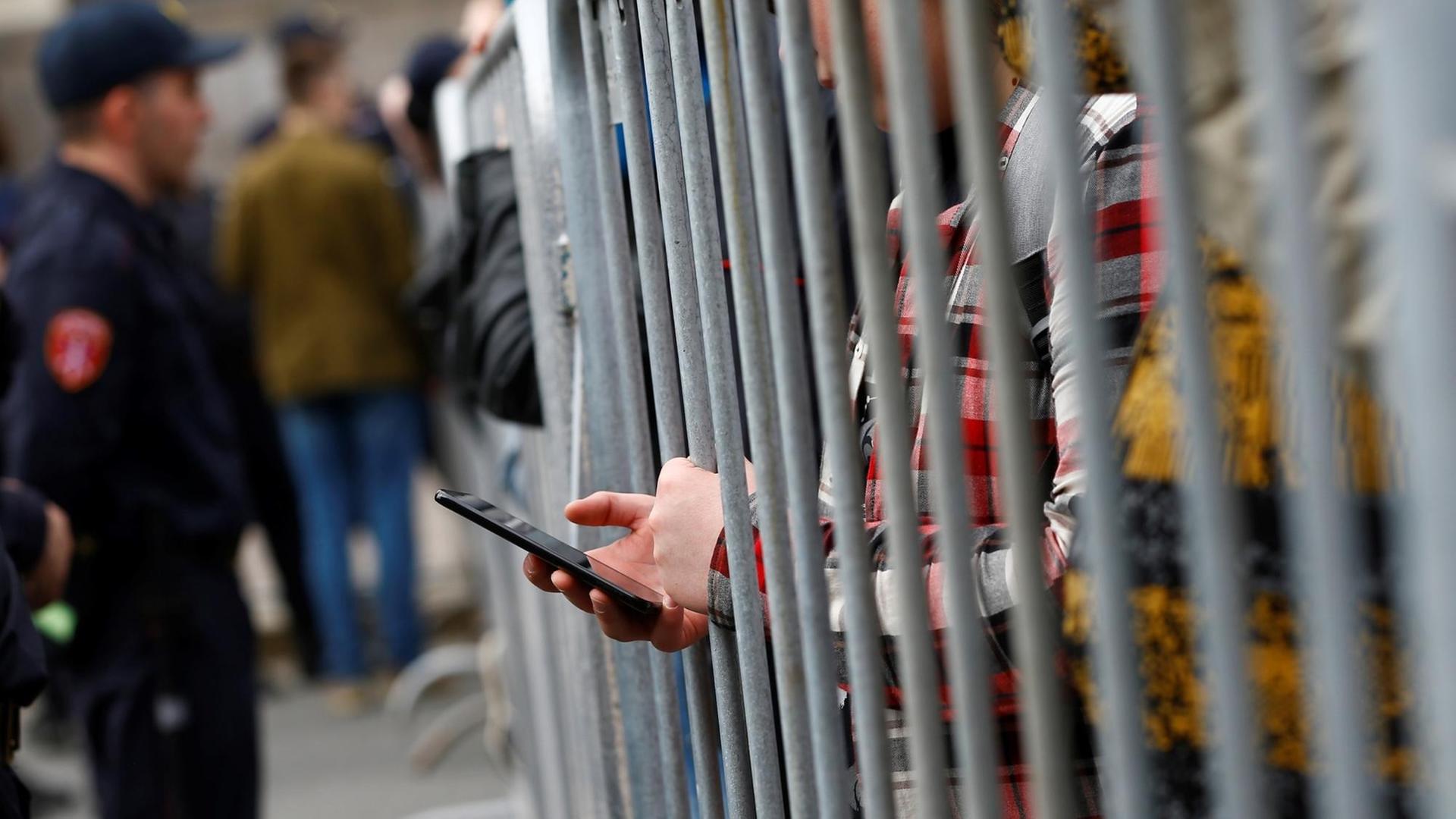 Ein Demonstrant in Moskau bedient sein Smartphone hinter einem Gitterzaun. Ein Demonstrant in Moskau bedient sein Smartphone hinter einem Gitterzaun.