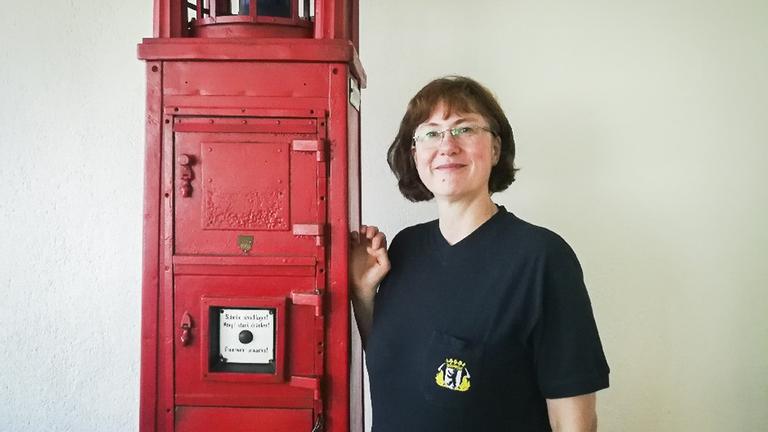 Sabine Röhm, die erste Feuerwehrseelsorgerin in Berlin, steht an einen roten Feuermelder gelehnt. Sabine Röhm, die erste Feuerwehrseelsorgerin in Berlin, steht an einen roten Feuermelder gelehnt.