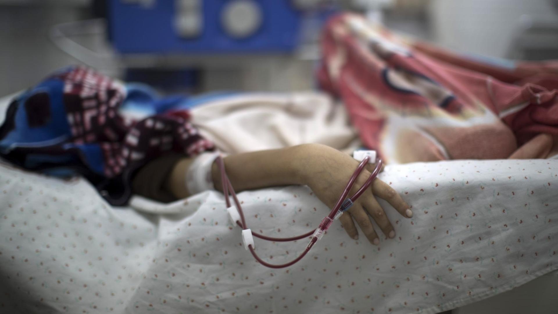 Eine Hand mit Schläuchen hängt aus einem Krankenbett. Eine Hand mit Schläuchen hängt aus einem Krankenbett.