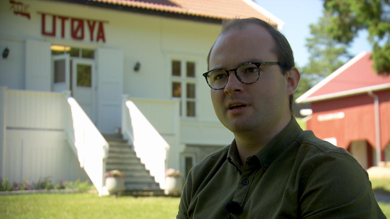 Ein Mann mit Brille, fliehender Stirn und glatt nach hinten gekämmtem Haar steht vor einem weißen Gebäude auf dem mit roten Buchstaben Utøya steht. Ein Mann mit Brille, fliehender Stirn und glatt nach hinten gekämmtem Haar steht vor einem weißen Gebäude auf dem mit roten Buchstaben Utøya steht.
