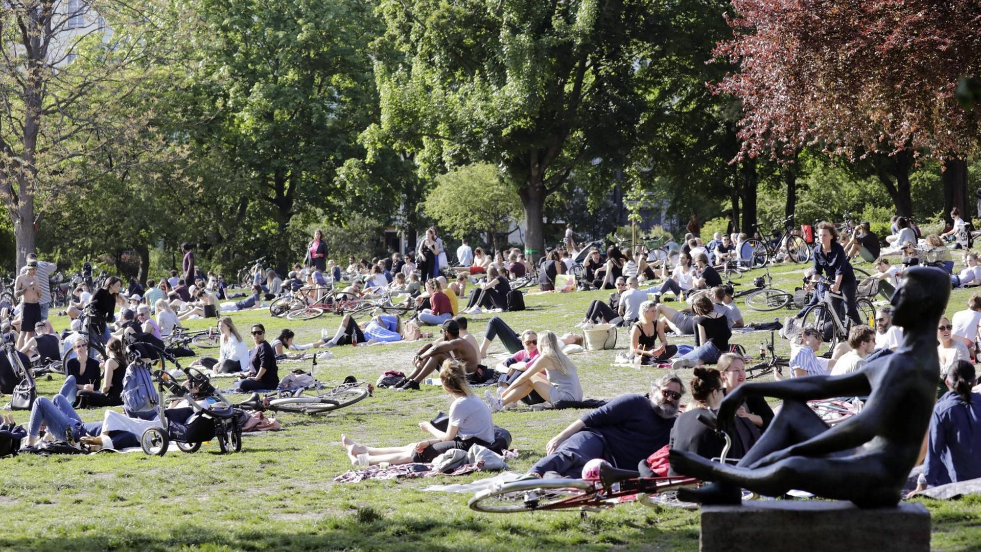Viele Menschen sonnen sich auf einer Wiese in einem Park